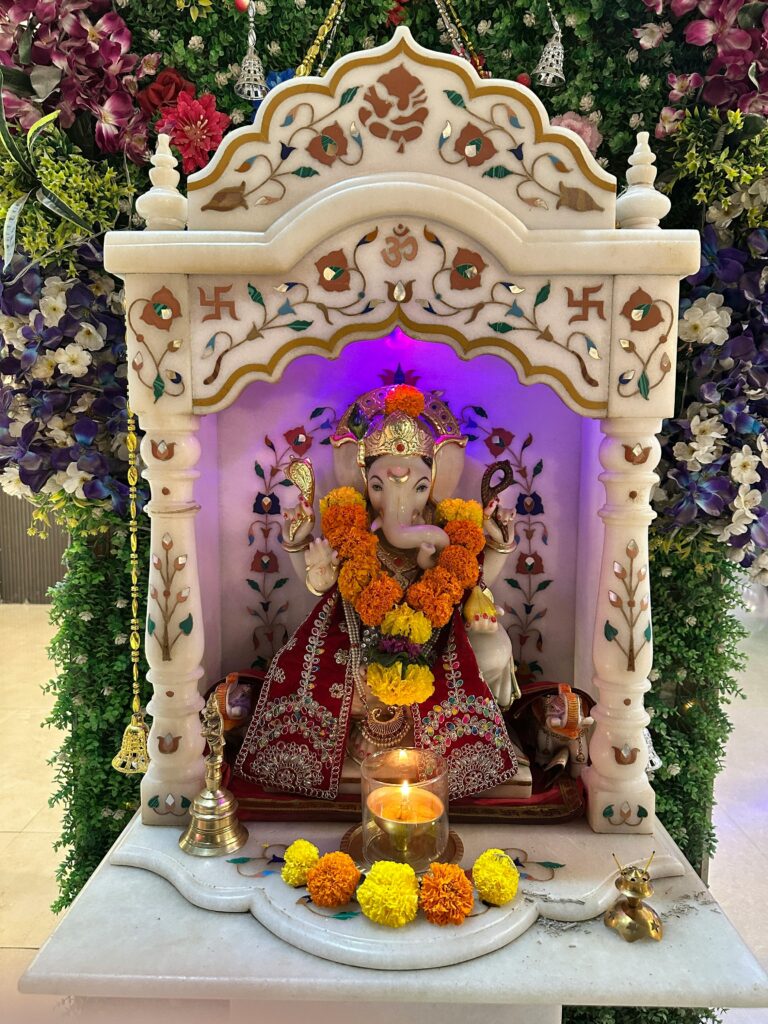 Intricately decorated Ganesh idol surrounded by vibrant flowers and glowing candles.